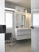 Blick ins helle Bad mit silbernem Mosaik und weißen Möbeln