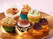 A selection of different luxury cupcakes on a gold plate sitting on a pink background
