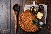 Cutting board, old wooden spoon, seasonings and parmesan cheese on dark wooden background