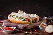 Homemade hot dogs on wooden plate with ingredients mustard, tomato sauce, onion, pepper, rosemary