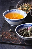 Grüntee, Teeperlen, Teeblume und aufgebrühter Tee in Teeschälchen