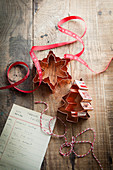 Copper christmas shaped cookie cutters on a rustic wooden surface with red Noel ribbon bakers twine and cookie recipe