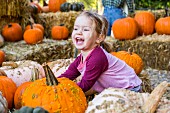 A young girl playing in a pumpkin patch and laughing