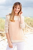 Blonde Frau in cremefarbenem Strickpullover und weißer Hose am Strand