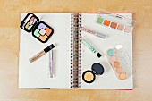 Various cosmetic products for colour-correcting laid out on a spiral-bound notebook