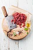 Raw chopped meat and meat cleaver on wooden cutting board on blue background