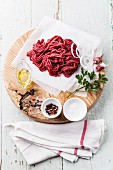 Fresh minced meat with onion and spices on wooden cutting board on blue background