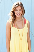 A blonde woman wearing a yellow summer dress and a long necklace