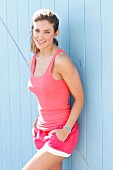 A brunette woman wearing a pink top and shorts in front of a blue wall