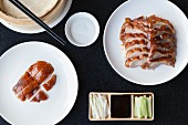 Slices of crispy Peking duck and duck skin with pancakes spring onions cucumber and hoisin sauce