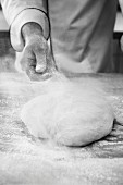 Bäcker bestäubt Brotteig mit Mehl