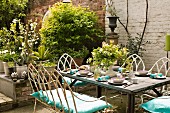 Gedeckter Tisch auf Terrasse vor Topfpflanzen und Gartenmauer