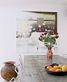 Vase of red roses on table in front of painting
