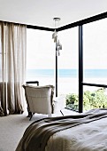 Designer lamp and armchair in the bedroom in front of a window with sea view