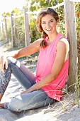 A young woman wearing a pink top and jeans with flower embroidery on the beach