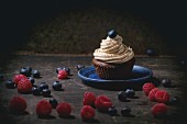 Chocolate cupcake with butter coffee cream and fresh berries over dark background