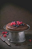 Chocolate cake with fresh berries and chocolate cream, served with vintage kitchenware over dark background