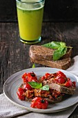 Italian tomato bruschetta with baked cherry tomatoes and fresh basil, served with glass of green smoothie
