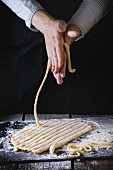 Female hands making pasta pici over wooden kitchen table, powdering by flour