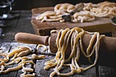 Fresh homemade pici pasta on wood chopping board over old wooden table with flour and rolling-pin
