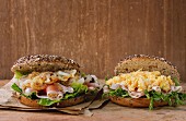Two Whole Grain bagels with fried onion, scrambled eggs, green salad and prosciutto ham on paper