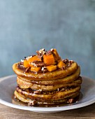 A stack of pumpkin pancakes with maple syrup and pecan nuts