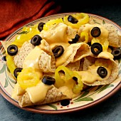 White corn tortilla chips with cheese sauce, black olives and banana peppers