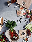 Frisches Gemüse, Gemüsesamen in Tütchen und Gartenwerkzeuge auf grauem Untergrund
