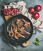 Grilled lamb meat chops with onion and rosemary in black cast iron pan served with fresh pomegranates