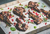 Grilled lamb ribs with pomegranate seeds, fresh mint and rosemary in metal baking tray