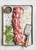 Raw uncooked roast beef meat cut with herbs, garlic and spices over light grey marble background