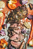Cooked Roast beef meat with roasted vegetables and herbs in metal baking tray, top view