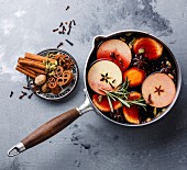 Mulled wine hot drink with citrus, apple and spices in aluminum casserole on concrete background