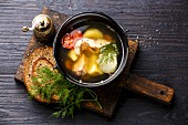 Fish soup with salmon, potato and carrot in black iron pot on black burned wooden background
