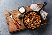 Fried potatoes roasted with porcini wild mushrooms in black iron pan on dark stone background