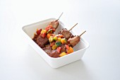Meat skewers with vegetable sauce in a takeaway box