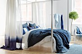 weiße Himmelbett mit Bettwäsche und Vorhang in Blau und Weiß in hellem Schlafzimmer