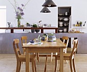 Oak table and chairs in front of elegant kitchen counter and stacked crockery on shelves in niche