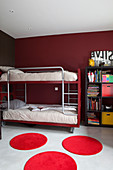 Bunk beds and bookcase in children's bedroom with dark red walls and round red rugs