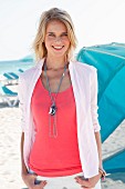 Blonde Frau in pinkfarbenem Top, weißer Hemdbluse und Halskette am Strand