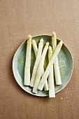 Cooked white asparagus spears with butter and salt on a plate (seen from above)