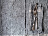Silberbesteck auf grauer Leinenserviette und Tischset