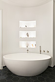 Oval free-standing bathtub against curved wall with niches