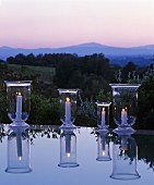 Lit candle lanterns reflected in surface of water in front of Mediterranean landscape