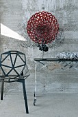 Designertisch mit schwarzer Fächerkoralle und roter Glasschale neben schwarzem Metallstuhl