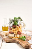 Lunch im Glas: Basilikum, Nudeln, getrocknete Tomaten, Oliven und Feta