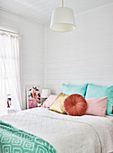Colourful cushions on bed in bedroom with board wall