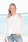 Blonde Frau in weißer Bluse mit Cut Outs und Jeans am Meer