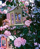 Tealight holders shaped like birdhouses amongst flowering roses