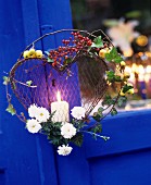 Pillar candle in wire love-heart decorated with ivy, branches and berries decorating summer garden